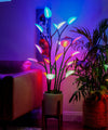 A floor plant lamp with multicolored lights resembling leaves, placed in a room with ambient lighting.