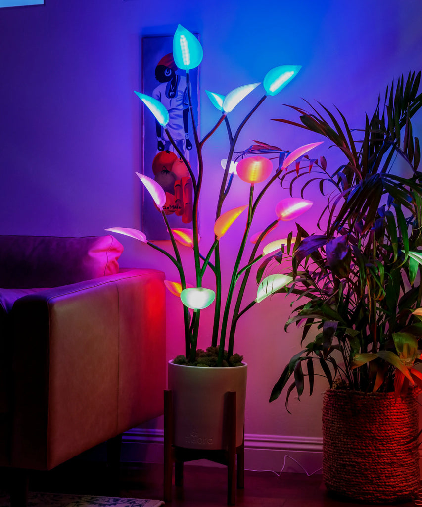 A floor plant lamp with multicolored lights resembling leaves, placed in a room with ambient lighting.