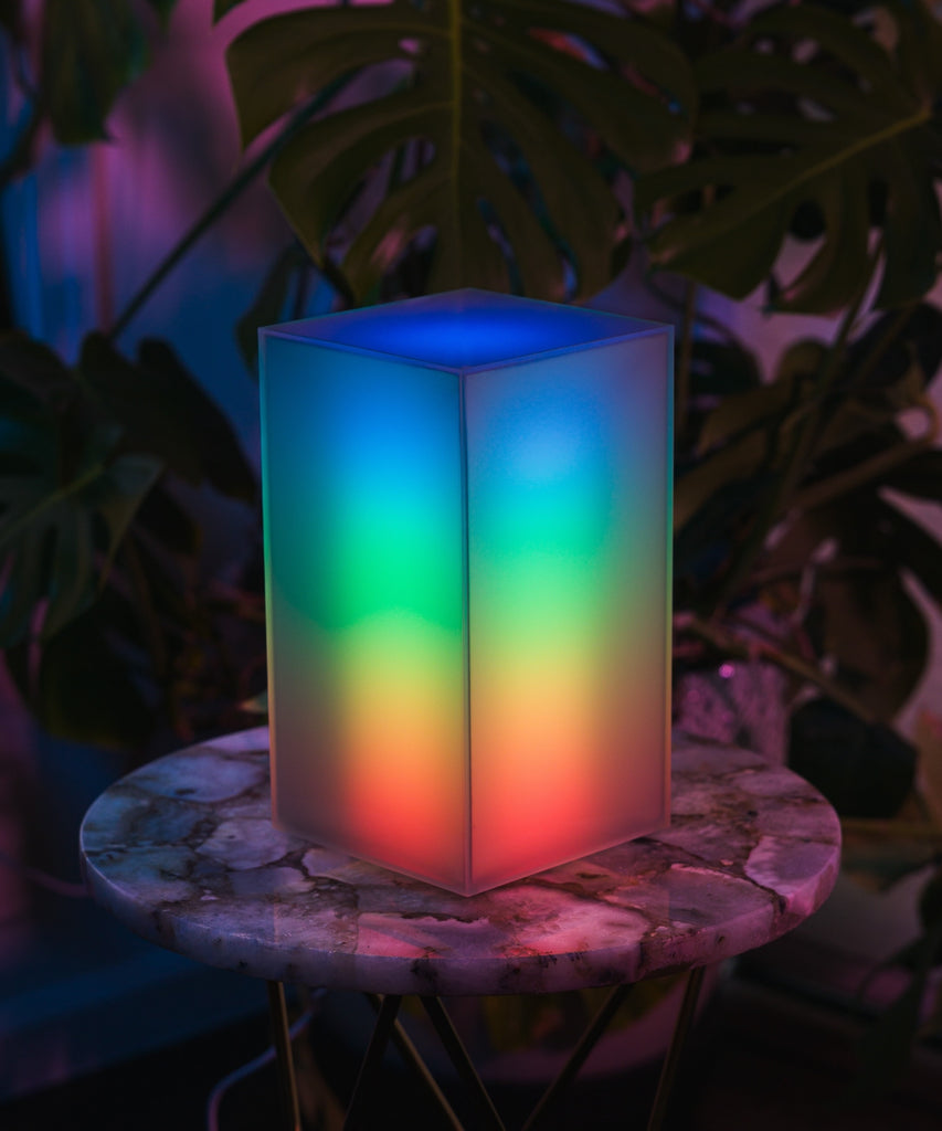 A modern designer lamp with a removable and customizable shade, radiating vibrant rainbow colors in a dark setting. Elevated Mood Light.
